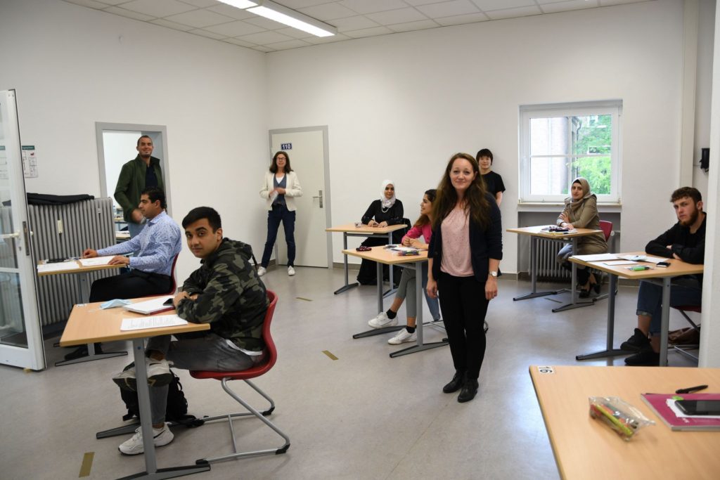 Fachbereichsleiterin Anna Epp und VHS-Leiterin Wilma Viol stehen im Klassenzimmer. An den Tischen sitzen Kursteilnehmer.