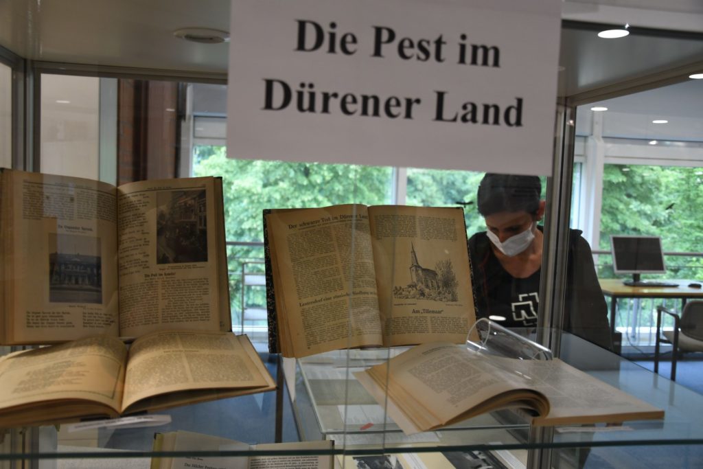 Quellen zum Thema Pest in Vitrine mit Betrachterin mit Munschutzmaske