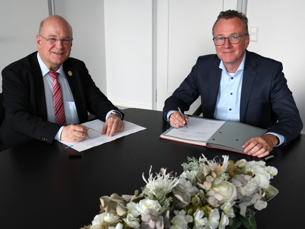Mit ihren Unterschriften besiegeln Bürgermeister Frank Peter Ullrich (li.) und Dr. Joachim Reichert (r.) die zukünftige weitere Zusammenarbeit.