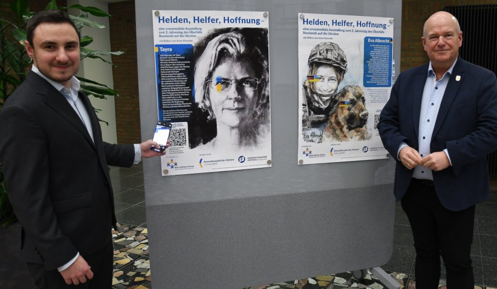 Bürgermeister Frank Peter Ullrich (r.) und Sebastian Eich, Partnerschaftsbeauftragter der Stadt Düren für die ukrainische Partnerstadt Stryj vor dem Plakat der Ausstellung im Foyer des Dürener Rathauses.