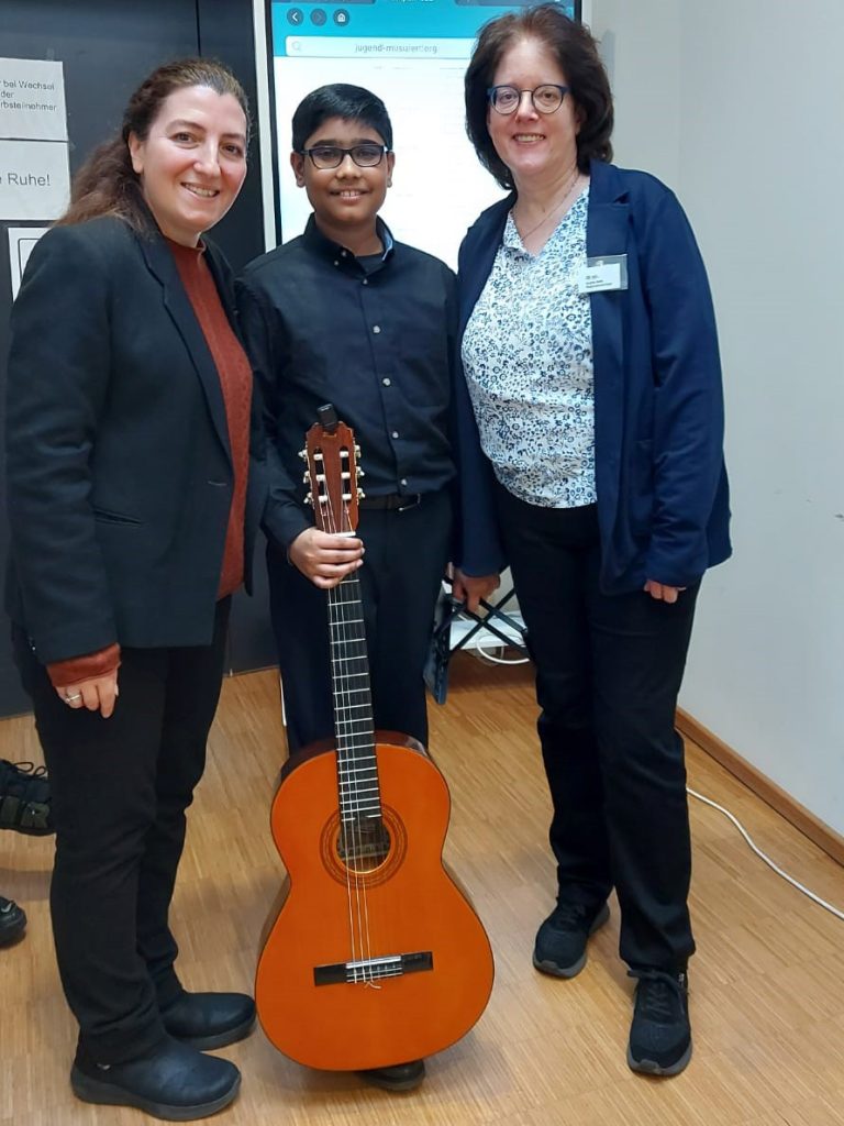 Gitarren-Lehrerin Melike Beser-Schneider (l.) und Andrea Nolte, die Leiterin der Musikschule Düren (r.) freuen sich zusammen mit Reyansh Sinha (Mitte) über dessen ersten Preis beim Landeswettbewerb von