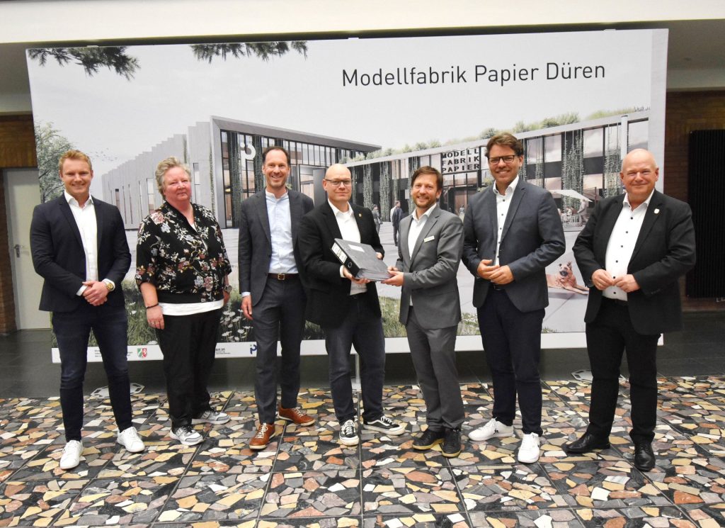 Gruppenfoto vor einer Leinwand mit einer Animation der Modelfabrik Papier