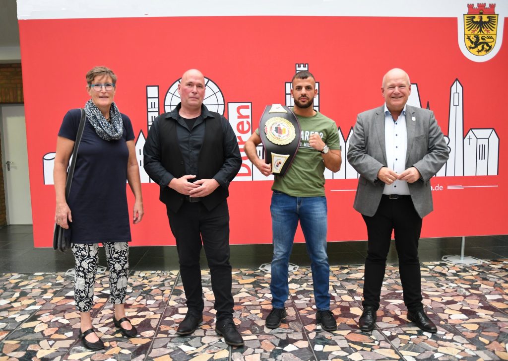 Gruppenfoto vor der Düren-Skyline. Yusuf Düskin steht neben Bürgermeister Frank Peter Ullrich unz zeigt seinen Championsgürtel