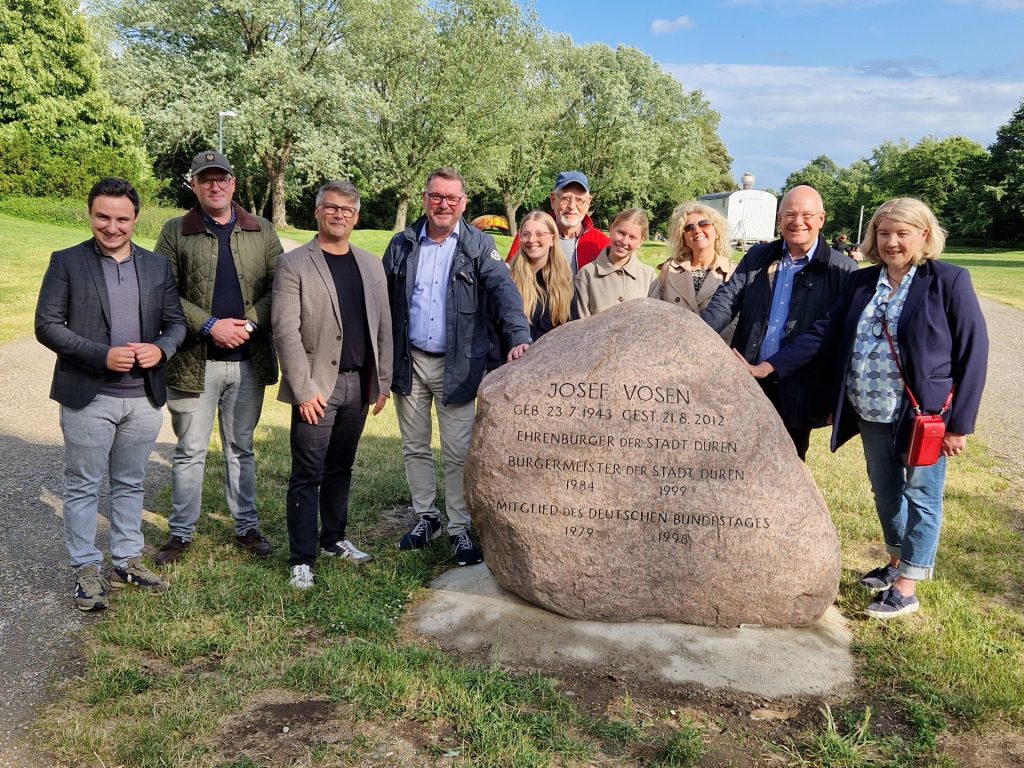 Gruppenfoto mit Gedenkstein im Vordergrund. Im Hintergrund ist das Parkgelände zu sehen.