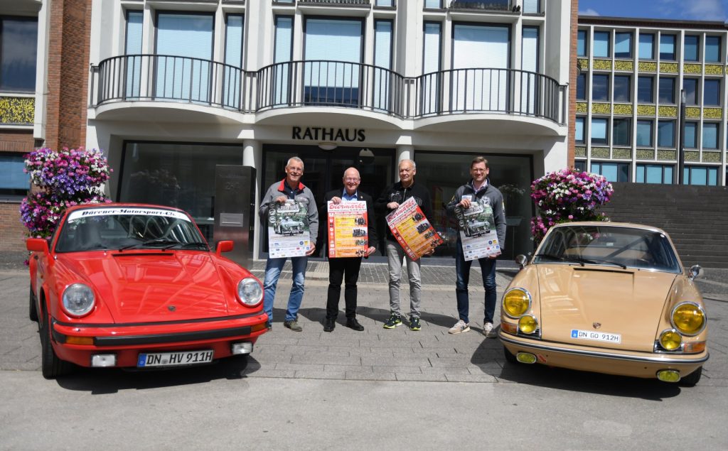 Gruppenfoto mit Plakaten vor dem Rathauseingang. Rechts und links stehen zwei Porsche-Oldtimer.