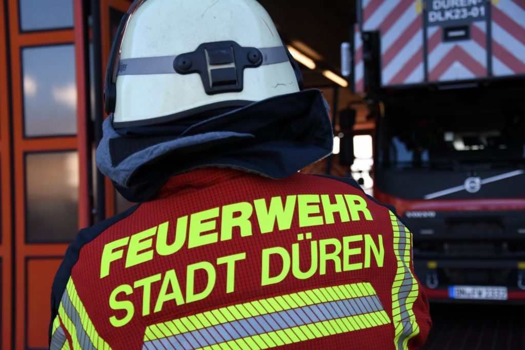 Feuerwehrmann vor der Wache mit Feuerwehrfahrzeug im Hintergrund