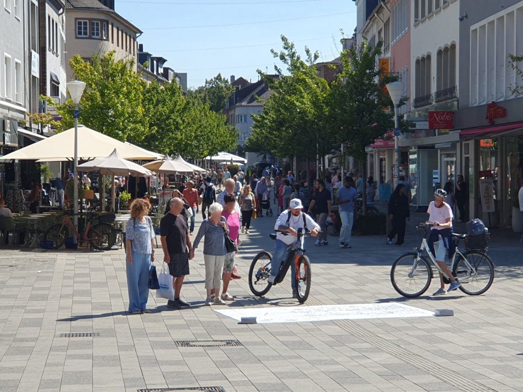 Menschen stehen auf dem Dürener Marktplatz vor einer Plane, die auf dem Boden liegt