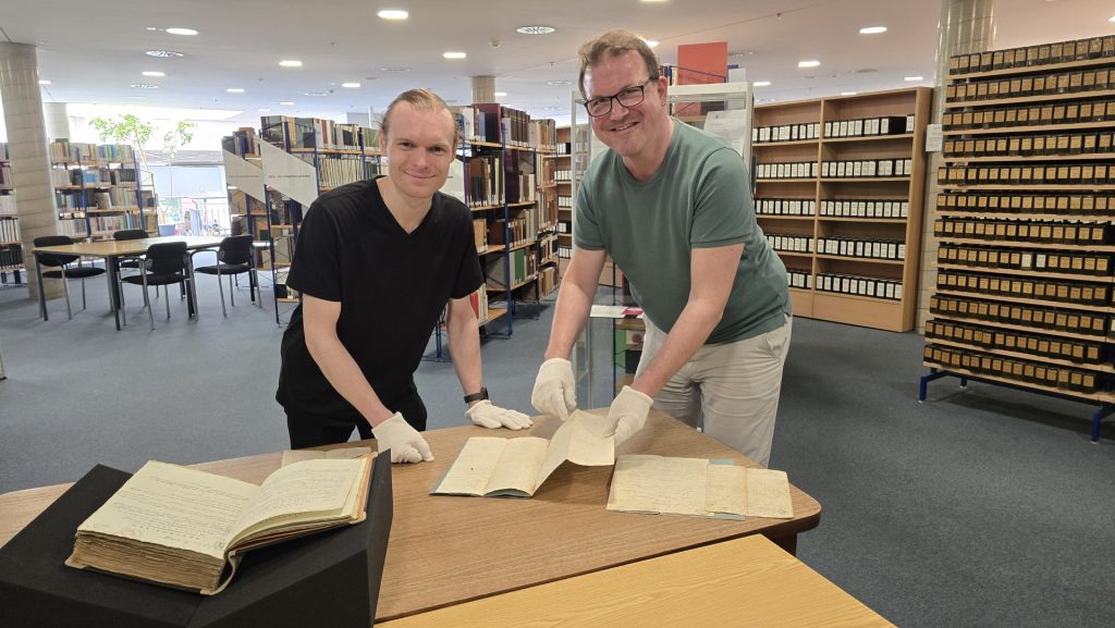 Das Foto zeigt Milan Reznik mit Archivleiter Daniel Schulte in den Räumen des Stadtarchivs beim Sichten alter Schriftstücke.