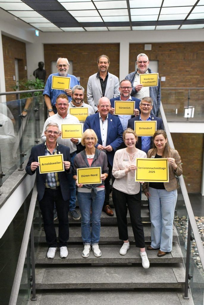 Gruppenfoto auf der Treppe im Rathausfoyer. Die Bezirksausschussvorsitzenden präsentieren dabei ihre Ortsschilder.