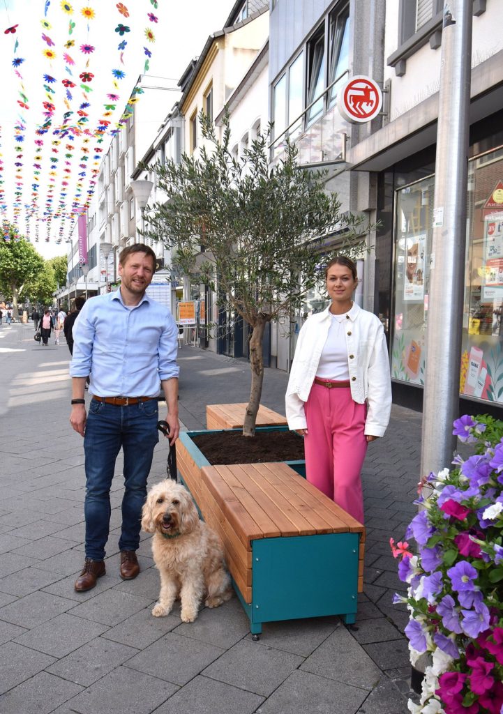 Das Foto zeigt Winfried Kranz-Pitre, Geschäftsführer der WIN.DN GmbH mit Hund und Laura Göttgens vom CityMa e.V. vor einer Bank.