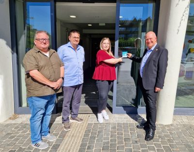 Das Foto zeigt unter anderem Jil Schulz und Bürgermeister Frank Peter Ullrich bei der Anbringung eines Aufklebers an der Eingangstür am Rathaus