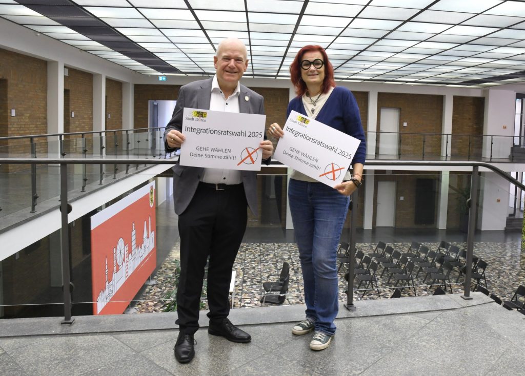 Bürgermeister Frank Peter Ullrich und Sabine Kieven halten jeweils ein Schild mit dem Aufruf, ihre Stimme abzugeben.