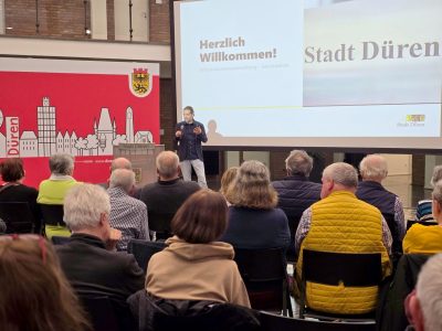 Ein Mann steht vor einem sitzenden Publikum und redet in ein Mikrofon
