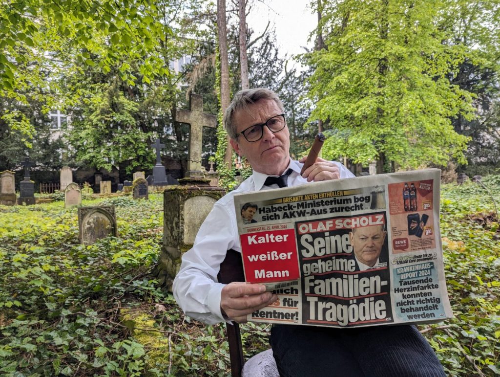 Ein Mann sitzt mit einer Zeitung in der Hand auf dem Friedhof