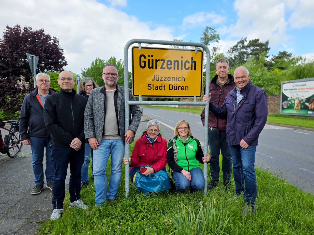 Gruppenbild mit Menschen an einem Ortseingangsschild