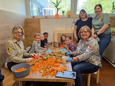 Kinder und Erwachsene sitzen um einen Tisch und bereiten Essen zu