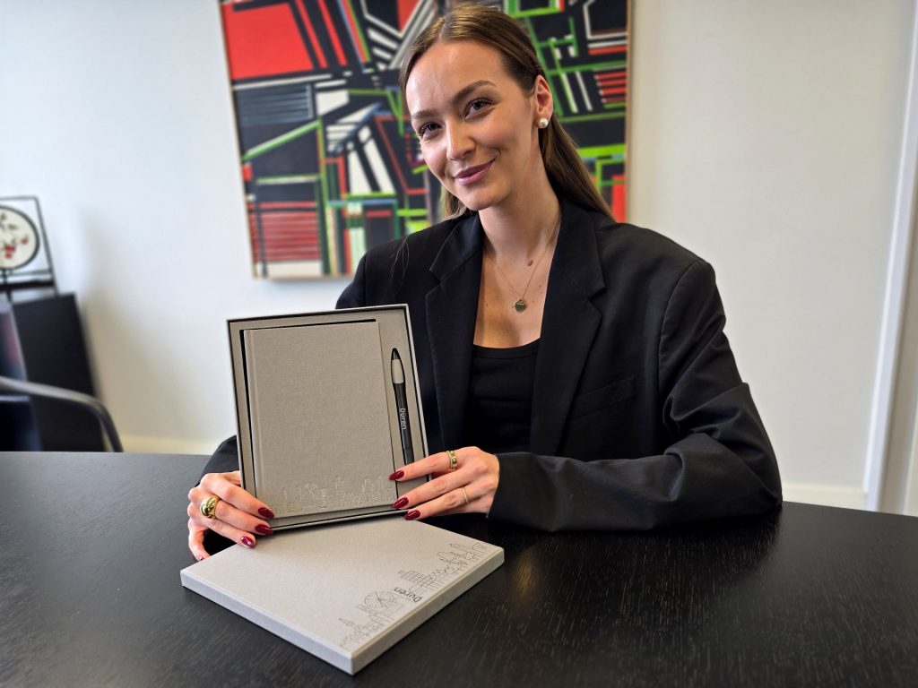 eine Frau sitzt an einem Tisch und zeigt ein Geschenkset in die Kamera