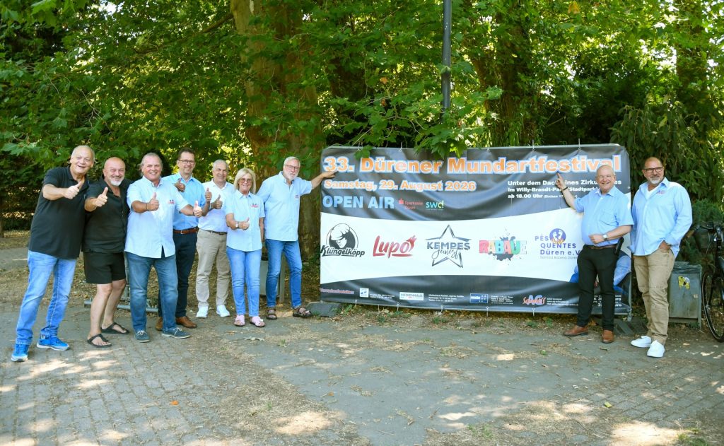 Gruppenfoto. Daziwischen ist ein Transparent mit Hinweisen zur Veranstaltung zu sehen.