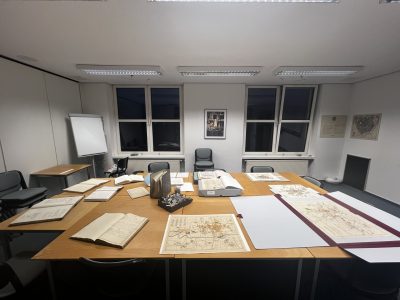 Zu sehen ist ein Raum des Stadt- und Kreisarchivs Düren. Auf einem Tisch liegen Bücher, Karten und Gegenstände.