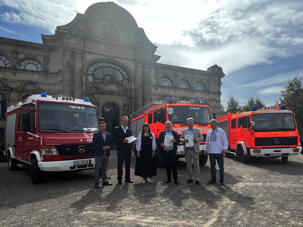 Gruppenbild mit Menschen und drei Feuerwehrfahrzeugen