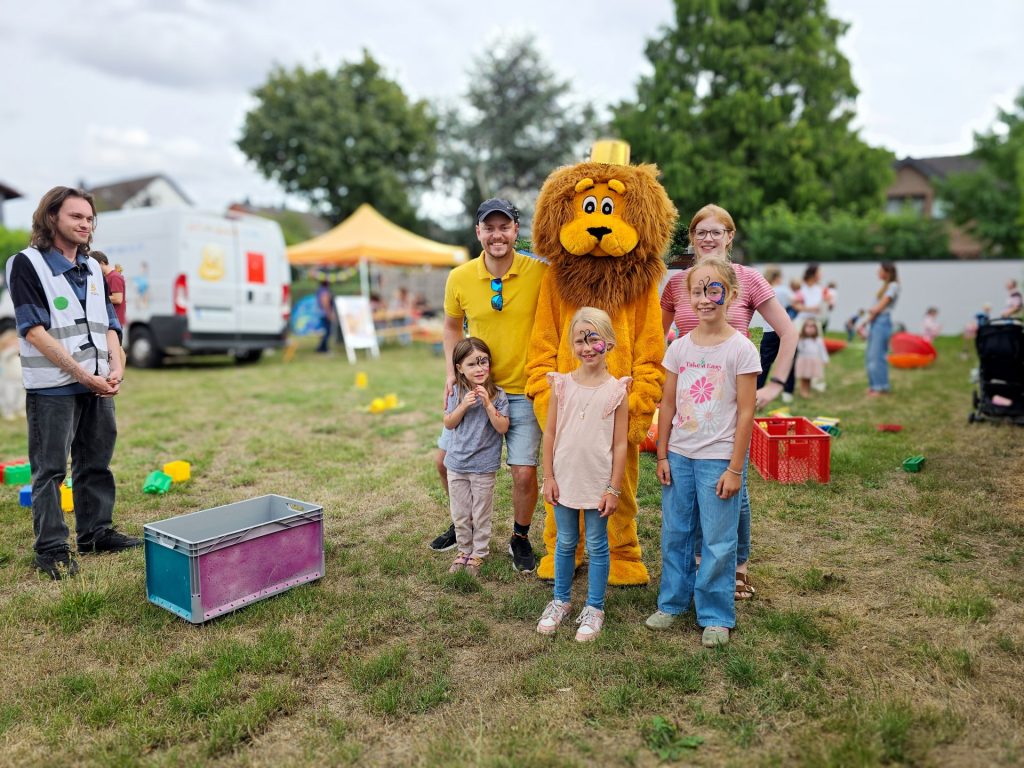 Gruppenbild mit Menschen und einem Maskottchen auf einem Spielplatz